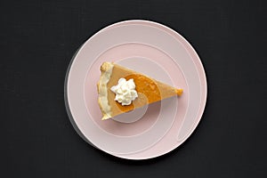 Homemade Thanksgiving pumpkin pie on a pink plate on a black surface, top view. Overhead, from above, flat lay. Close-up