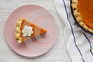 Homemade Thanksgiving pumpkin pie on a pink plate on a white wooden table, overhead view. Top view, from above, flat lay