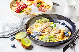 Homemade thin crepes served with curd cream, fruits and berries in black and white plates