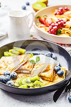 Homemade thin crepes served with curd cream, fruits and berries in black and white plates