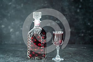 Homemade tincture of red cherry in a glass bottle and a wine crystal glass , Ukraine, close up