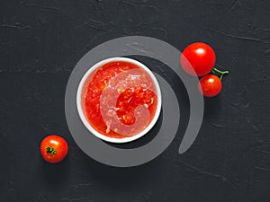 Homemade tomato sauce made from fresh ripe tomatoes in white bowl on black background. Vegetarian food. Top view