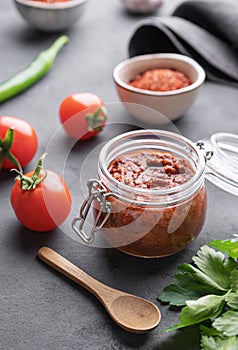 Homemade tomato sauce for pizza or pasta in a jar on a dark background with fresh vegetables, herbs and spicy close up