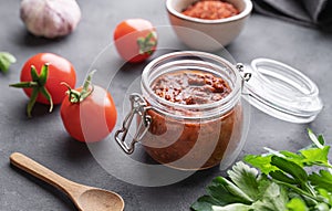 Homemade tomato sauce for pizza or pasta in a jar on a dark background with fresh vegetables, herbs and spicy close up
