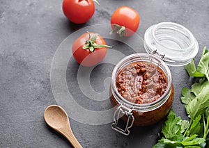 Homemade tomato sauce for pizza or pasta in a jar on a gray background with fresh vegetables and herbs.