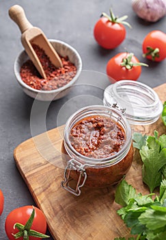 Homemade tomato sauce for pizza or pasta in a jar on a gray background with fresh vegetables, herbs and spicy
