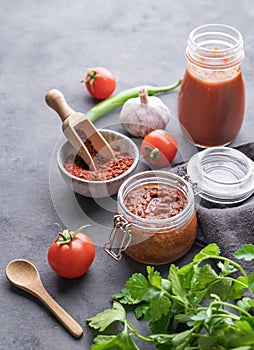 Homemade tomato sauce for pizza or pasta in a jar on a gray background with fresh vegetables, herbs and spicy