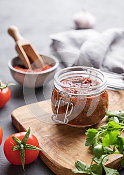 Homemade tomato sauce for pizza or pasta in a jar on a gray background with fresh vegetables, herbs and spicy close up