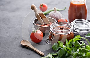Homemade tomato sauce for pizza or pasta in a jar on a gray background with fresh vegetables, herbs and spicy. The concept of