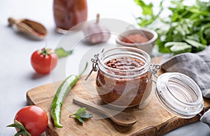 Homemade tomato sauce for pizza or pasta in a jar on a light background with fresh vegetables and herbs close up