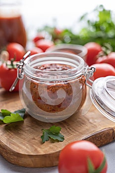 Homemade tomato sauce for pizza or pasta in a jar on a light background with fresh vegetables and herbs close up