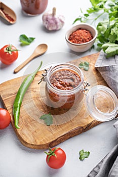 Homemade tomato sauce for pizza or pasta in a jar on a wooden board on a light background with fresh vegetables and herbs