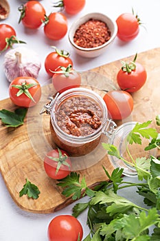 Homemade tomato sauce for pizza or pasta in a jar on a wooden board on a light background with fresh vegetables and herbs close up