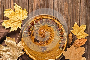 Homemade traditional pumpkin pie decorated with nuts and seeds. Natural rustic style wooden background.