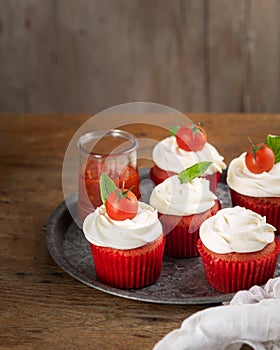 Homemade unsweetened savory appetizer cupcakes snacks with cream cheese frosting, tomato and fresh basil over wooden background,