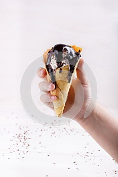 Homemade vanilla ice-cream with chocolate topping in waffle cone held in the hand on white