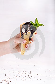 Homemade vanilla ice-cream with chocolate topping in waffle cone held in the hand on white