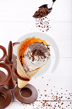 Homemade vanilla ice-cream with chocolate topping in waffle cone on white table