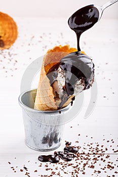 Homemade vanilla ice-cream with chocolate topping in waffle cone on white table