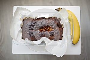 Homemade vegan baked banana bread on parchment paper just out of the oven on a white cutting board