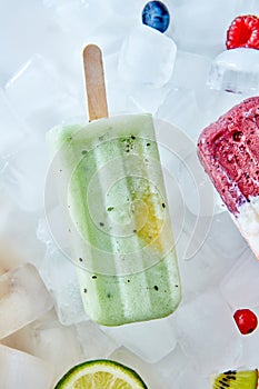 Homemade vegan frozen kiwi popsicles over the ice with slice lime, berries and kiwi, flat lay