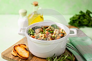 Homemade vegetable soup with meatballs and spinach in a white saucepan on a green background.