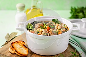 Homemade vegetable soup with meatballs and spinach in a white saucepan on a green background.