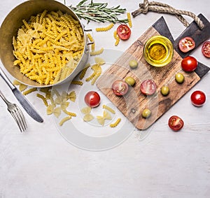 Homemade vegetarian pasta laid out in the bowl, with herbs, oil, olives, cherry tomatoes on a wooden board , place for t