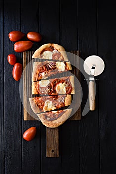 Homemade vegetarian pizza. Freshly baked oval pizza with tomatoes and bell peppers on black background top view