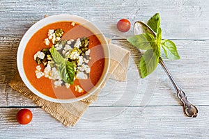 Homemade vegetarian tomato soup with feta cheese and pesto sauce in white bowl on wooden background