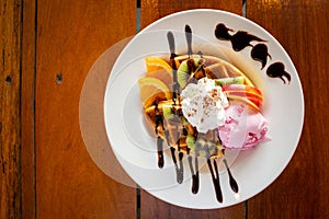 Homemade waffle served with stawberry ice cream and variety fruit. Sweet and crunchy dessert.