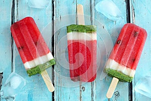 Homemade watermelon popsicles with ice against rustic blue wood