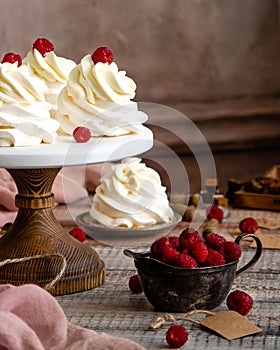 Homemade white mini desserts pavlova on wooden cake stand with whipped cream and raspberries on grey table with pink cloth