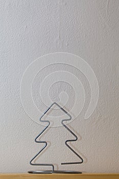 A homemade wire Christmas tree sits on a wooden shelf with white wallpaper symbolizing winter and snow.