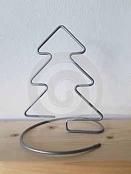 A homemade wire Christmas tree sits on a wooden shelf with white wallpaper symbolizing winter and snow.
