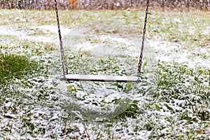 Homemade wooden swing covered first snow at winter on natural background. Loneliness concept