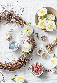 Homemade wreath with flowers and accessories for crafts creativity on a light background, top view.