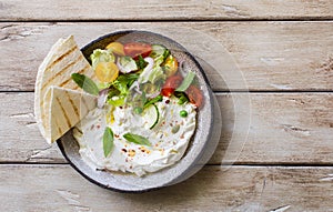 Homemade yogurt cheese labneh with raw vegetable salad and lavash bread served on rustic plate
