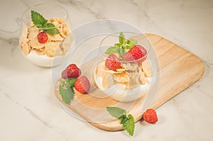 Homemade yogurt with corn flakes, strawberry and mint/ Smoothies with corn flakes decorated mint and strawberry on white table