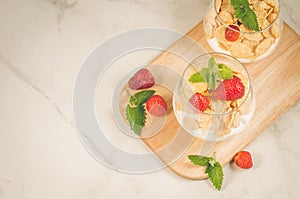 Homemade yogurt with corn flakes, strawberry and mint/Smoothies with corn flakes decorated mint and strawberry on white table. Top