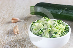 Homemade zucchini spaghetti in white bowl with garlic