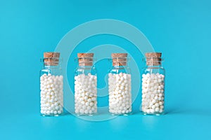 Homeopathic globules in four glass bottles on blue background. Alternative homeopathy medicine herbs, healthcare and