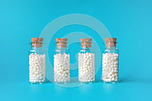 Homeopathic globules in four glass bottles on blue background. Alternative homeopathy medicine herbs, healthcare and photo
