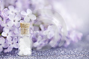 Homeopathic globules in glass bottle, close-up on a background of lilac flowers. Selective focus. Alternative medicine concept.