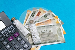 Homeopathic globules in glass bottles, calculator and Indian currency on blue background.Homeopathic Medicine and money concept