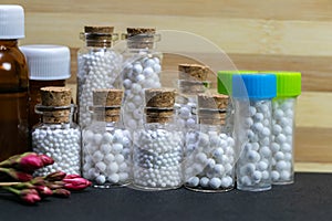 Homeopathic medicine bottles consisting of pills and liquid substance with pink flower bud on wood and dark background. Natural