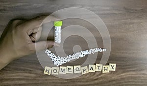 A homeopathy concept â€“ Holding Homeopathic medicine bottle in hand with Homeopathy text and tick mark of globules on wood