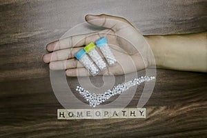 Homeopathy concept â€“ Man hand holding three bottles of Homeopathic medicines and tick mark of scattered globules with Homeopathy