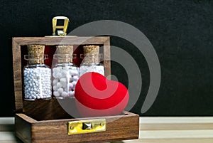 Homeopathy â€“ Close view of homeopathy medicine bottles with cork and heart in wooden old box on wood and dark background.