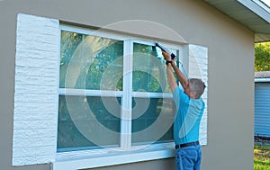 Homeowner caulking window weatherproofing home against rain and storms